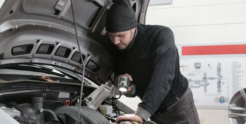 A man is focused on fixing a car inside a garage, with various tools visible around him.